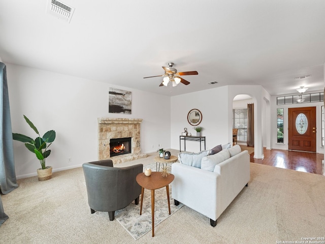 living room featuring baseboards, visible vents, arched walkways, and a stone fireplace