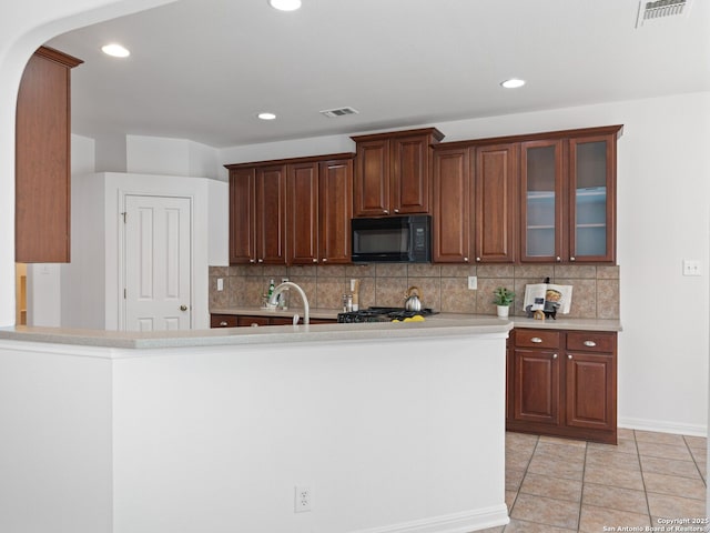 kitchen featuring light countertops, visible vents, decorative backsplash, glass insert cabinets, and black microwave