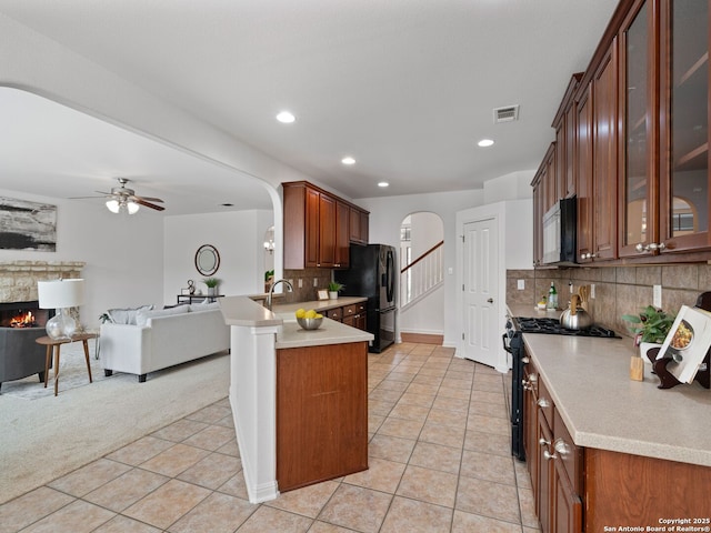 kitchen with light countertops, glass insert cabinets, open floor plan, a peninsula, and black appliances