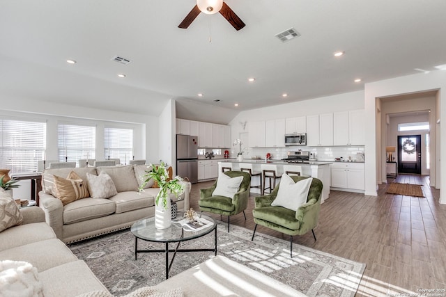 living room with ceiling fan, light hardwood / wood-style flooring, and vaulted ceiling