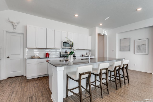 kitchen featuring dark wood-type flooring, a breakfast bar area, an island with sink, white cabinetry, and stainless steel appliances