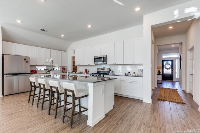 kitchen with white cabinetry, tasteful backsplash, a breakfast bar area, a center island with sink, and appliances with stainless steel finishes