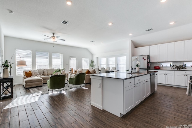 kitchen featuring tasteful backsplash, white cabinets, refrigerator, and an island with sink