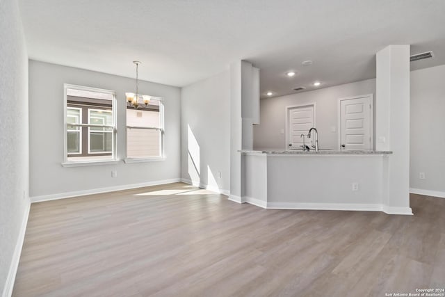 unfurnished living room with light wood-type flooring, a notable chandelier, and sink