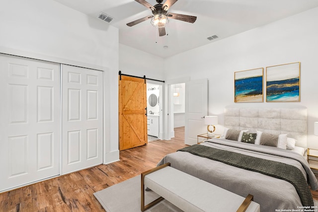 bedroom featuring ceiling fan, a barn door, a closet, and light hardwood / wood-style flooring