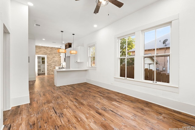 unfurnished living room with hardwood / wood-style flooring, ceiling fan, and brick wall