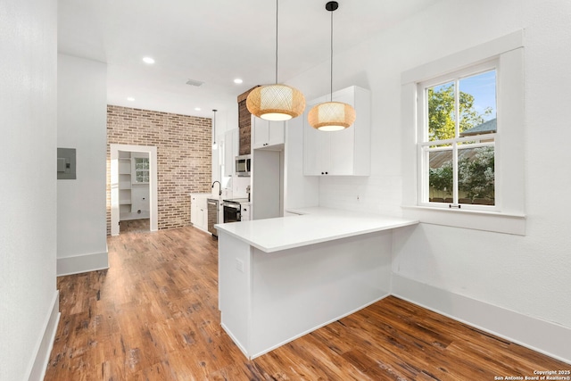 kitchen with white cabinetry, brick wall, kitchen peninsula, pendant lighting, and appliances with stainless steel finishes