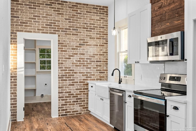 kitchen with white cabinets, appliances with stainless steel finishes, decorative light fixtures, and brick wall