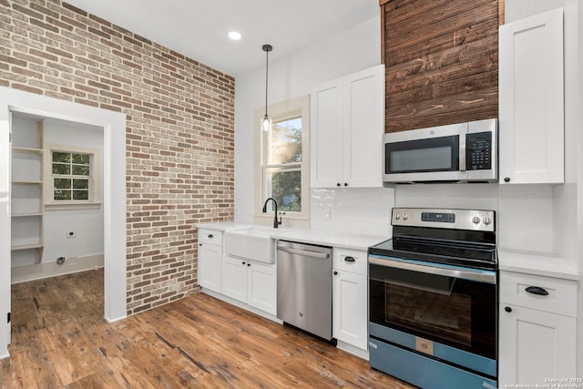 kitchen featuring pendant lighting, white cabinets, stainless steel appliances, and brick wall