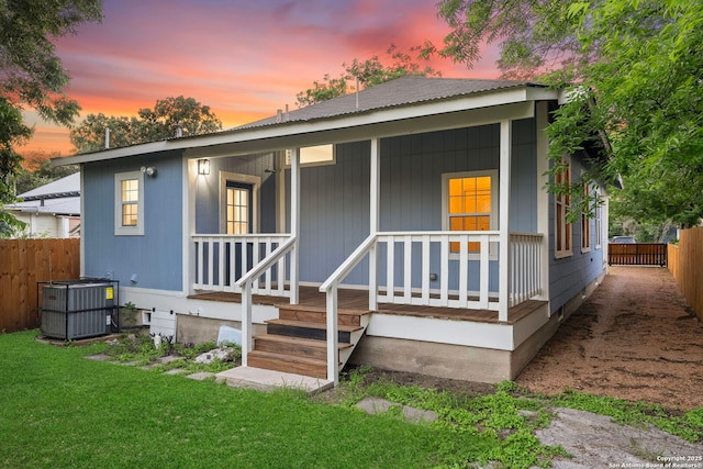 back house at dusk with central AC unit, a porch, and a yard