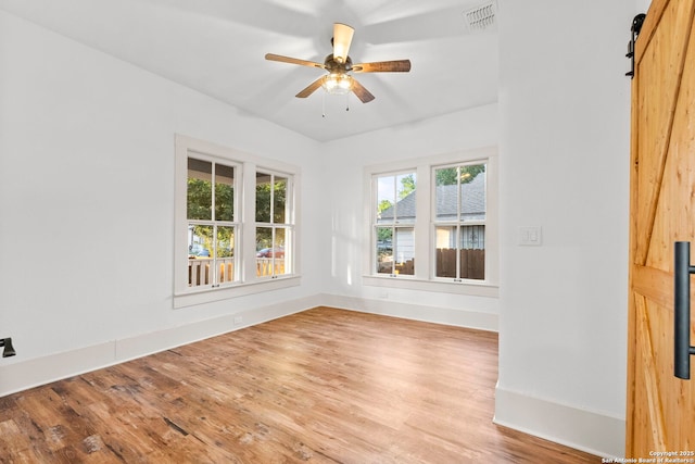 spare room with a barn door, hardwood / wood-style flooring, and ceiling fan