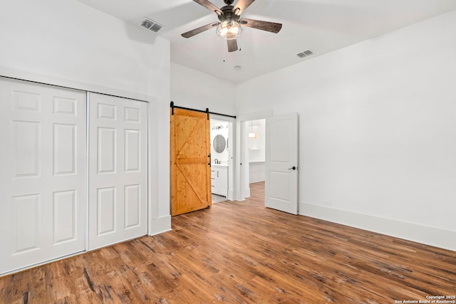 unfurnished bedroom featuring a barn door, ceiling fan, a closet, and hardwood / wood-style flooring