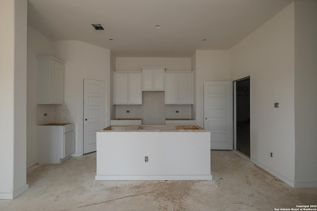 kitchen featuring white cabinets, unfinished concrete flooring, tasteful backsplash, and a kitchen island