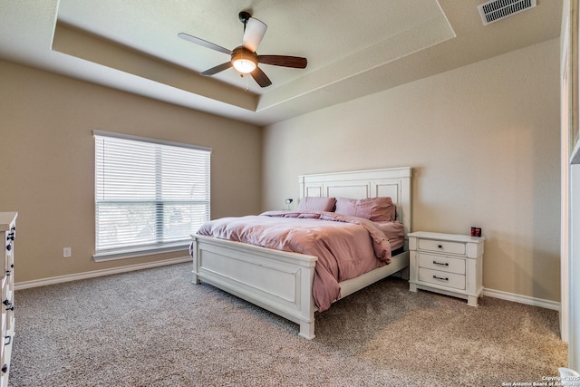 carpeted bedroom with a tray ceiling and ceiling fan