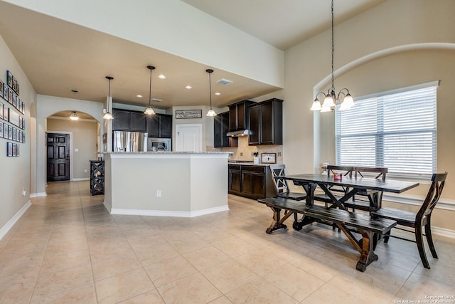 kitchen with stainless steel fridge, tasteful backsplash, a center island with sink, a chandelier, and hanging light fixtures