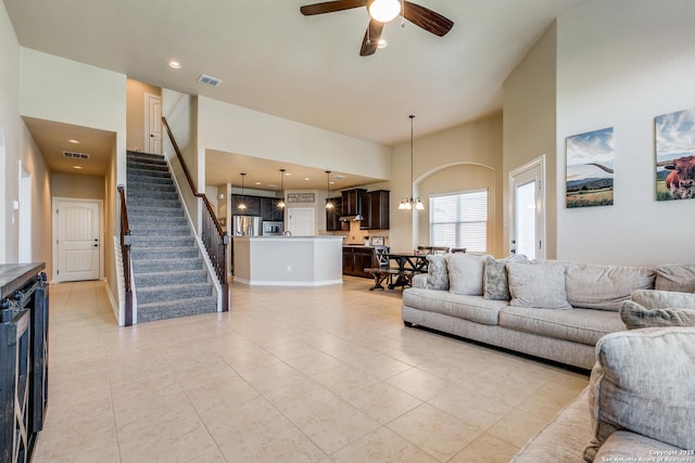 tiled living room featuring beverage cooler, a high ceiling, and ceiling fan with notable chandelier