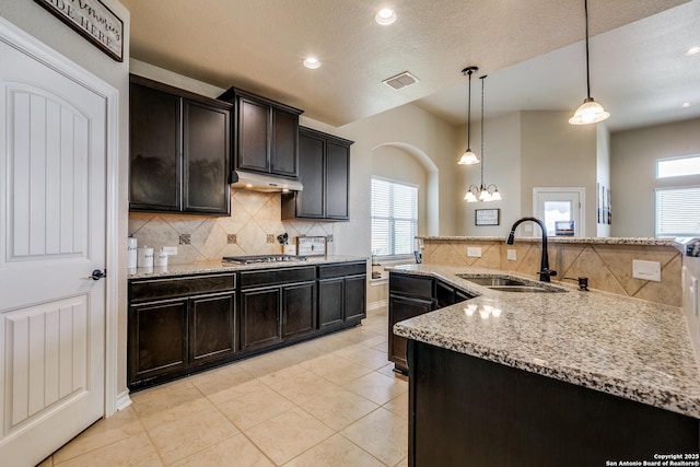 kitchen with stainless steel gas stovetop, sink, light tile patterned floors, tasteful backsplash, and decorative light fixtures