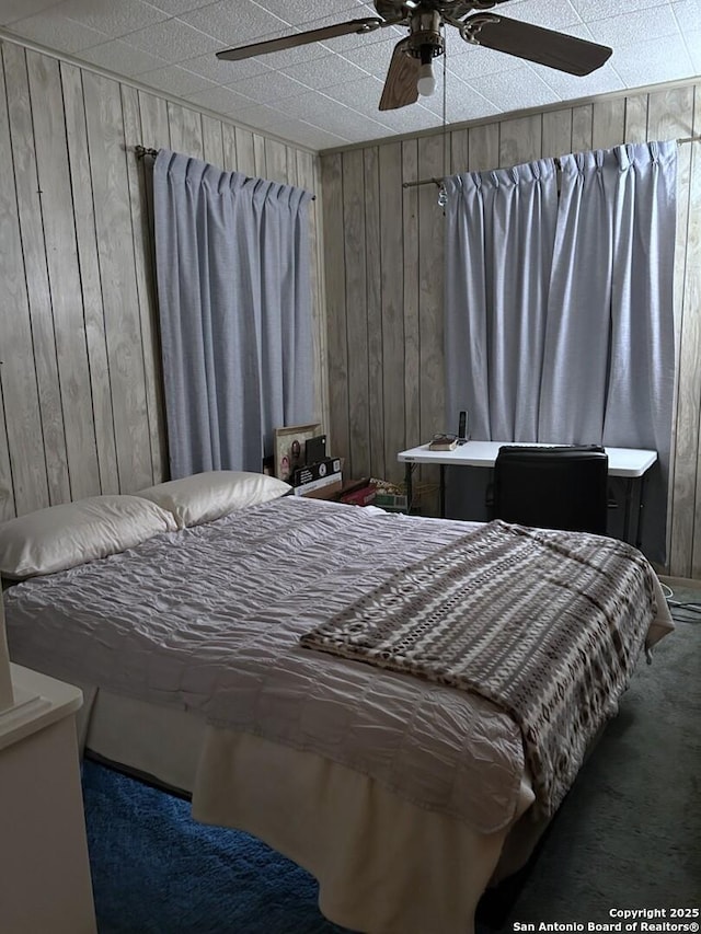 bedroom featuring dark colored carpet, ceiling fan, and wooden walls