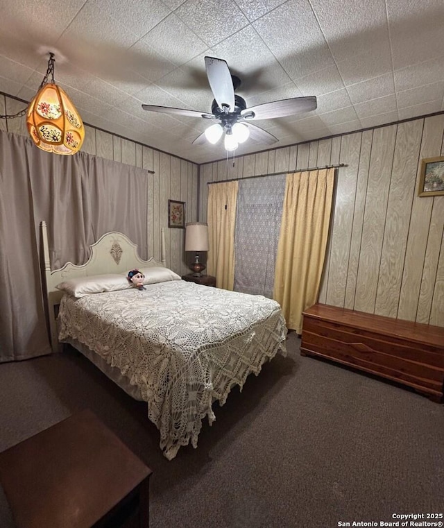 carpeted bedroom with ceiling fan and wood walls