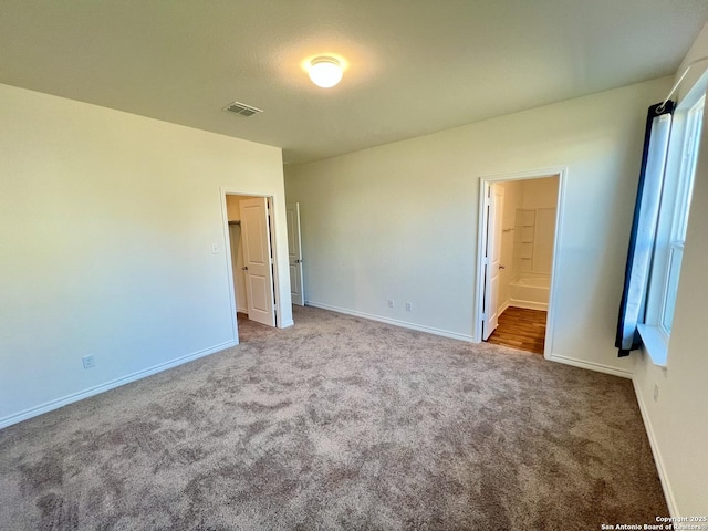 unfurnished bedroom featuring carpet flooring, ensuite bath, and a spacious closet