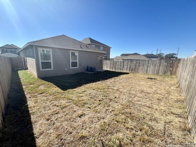 rear view of house with central AC and a yard