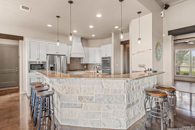 kitchen with decorative backsplash, appliances with stainless steel finishes, light stone countertops, white cabinetry, and hanging light fixtures