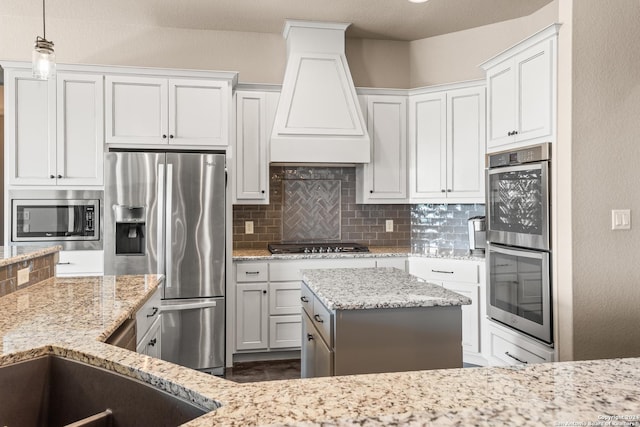 kitchen featuring backsplash, custom range hood, stainless steel appliances, white cabinetry, and hanging light fixtures