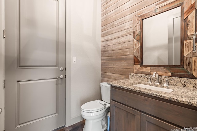 bathroom with vanity, toilet, and wood walls