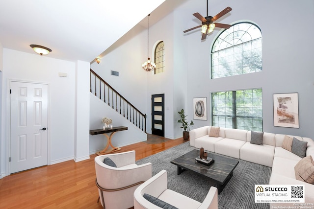 living room with light wood-type flooring, ceiling fan with notable chandelier, and a towering ceiling