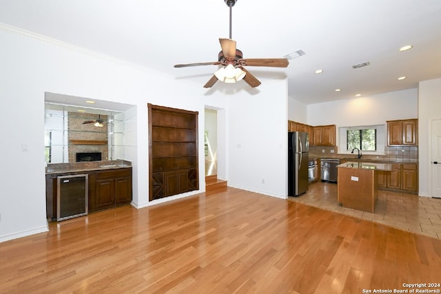 kitchen featuring appliances with stainless steel finishes, wine cooler, ceiling fan, backsplash, and a brick fireplace