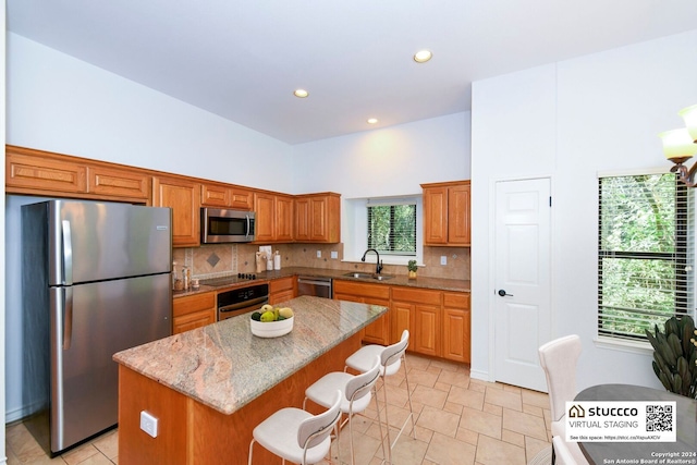 kitchen with appliances with stainless steel finishes, sink, a kitchen island, a breakfast bar, and light stone counters