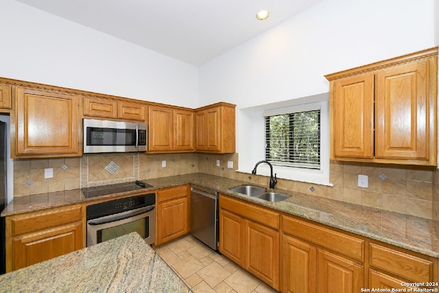 kitchen with sink, a towering ceiling, light stone counters, decorative backsplash, and stainless steel appliances