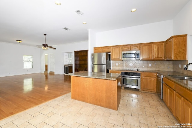 kitchen with ceiling fan, sink, dark stone counters, a kitchen island, and stainless steel appliances