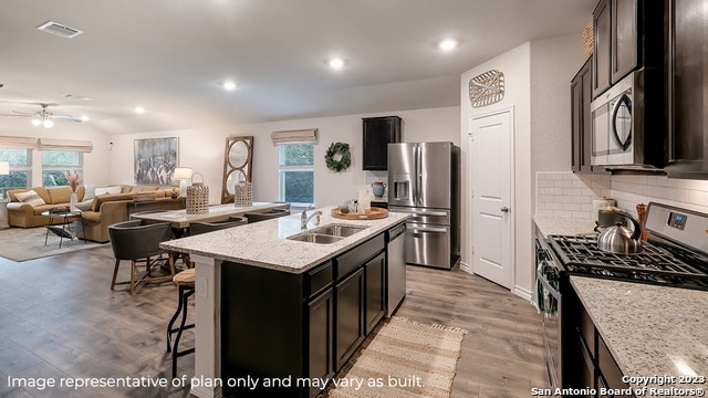 kitchen with light stone countertops, sink, stainless steel appliances, tasteful backsplash, and a center island with sink