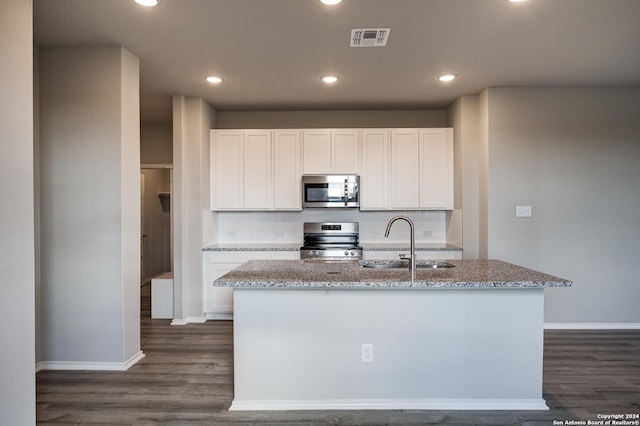 kitchen featuring white cabinets, stainless steel appliances, light stone countertops, and a center island with sink