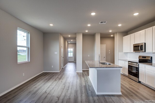 kitchen featuring white cabinets, light stone countertops, stainless steel appliances, and an island with sink