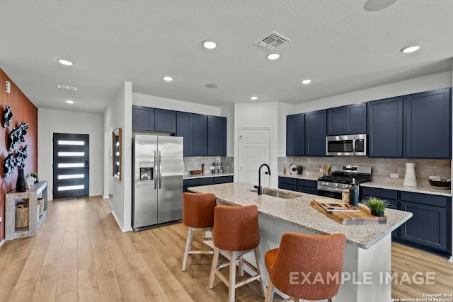 kitchen with a center island with sink, sink, light stone countertops, and stainless steel appliances