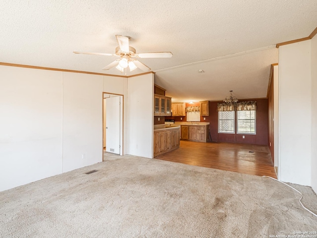 unfurnished living room with ceiling fan with notable chandelier, a textured ceiling, crown molding, carpet floors, and lofted ceiling