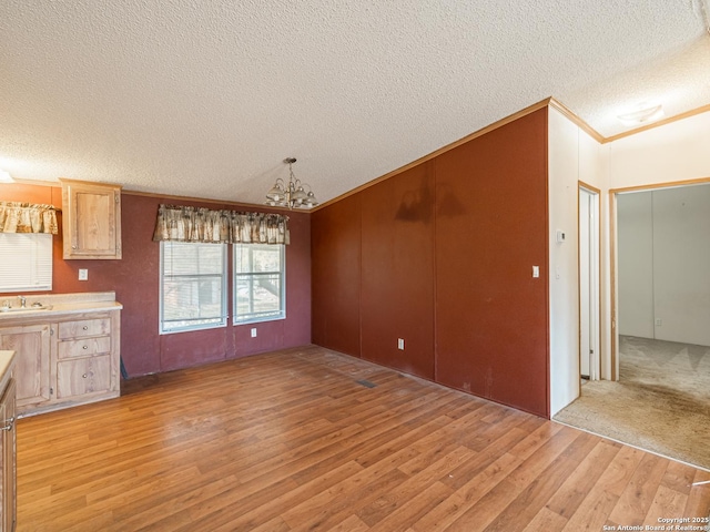 unfurnished dining area featuring light hardwood / wood-style flooring, a chandelier, a textured ceiling, and sink