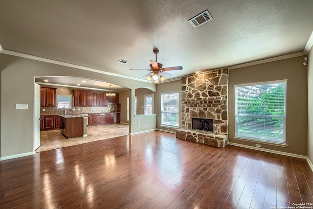 unfurnished living room featuring ceiling fan with notable chandelier, crown molding, light wood-type flooring, and a fireplace