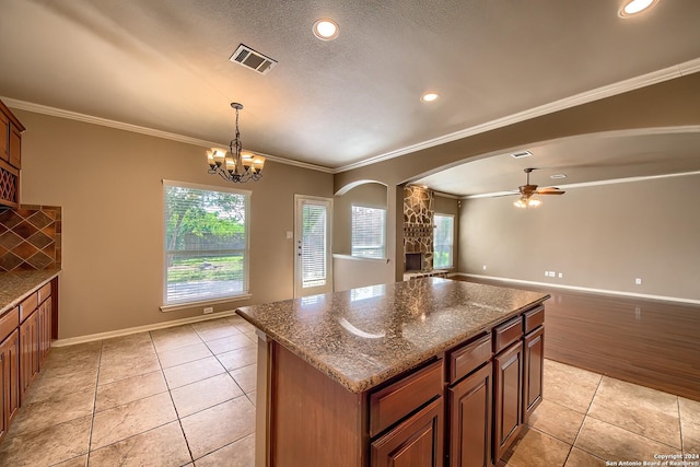 kitchen featuring stone counters, a center island, crown molding, light tile patterned floors, and ceiling fan with notable chandelier