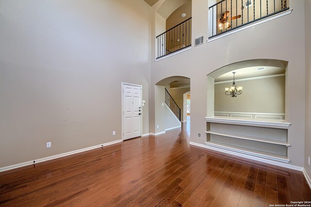 unfurnished living room featuring hardwood / wood-style flooring, a notable chandelier, and a towering ceiling