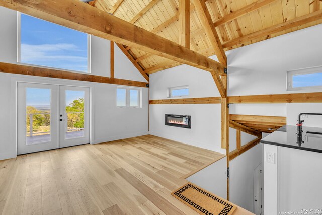 unfurnished living room featuring beam ceiling, french doors, high vaulted ceiling, and light hardwood / wood-style floors