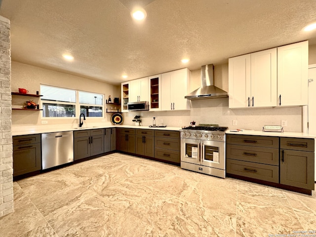 kitchen featuring wall chimney exhaust hood, a textured ceiling, stainless steel appliances, sink, and white cabinets