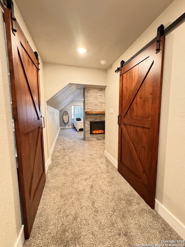 additional living space with a barn door, a fireplace, carpet, and a textured ceiling