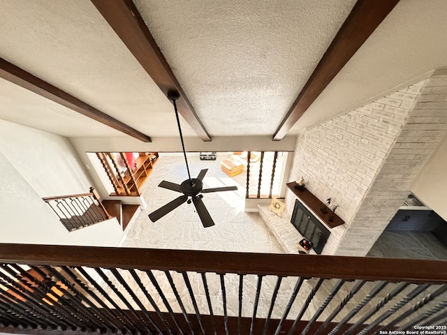 staircase featuring ceiling fan, a fireplace, beamed ceiling, and a textured ceiling