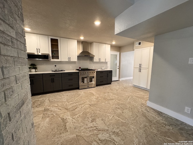 kitchen with a textured ceiling, white cabinetry, double oven range, and wall chimney range hood