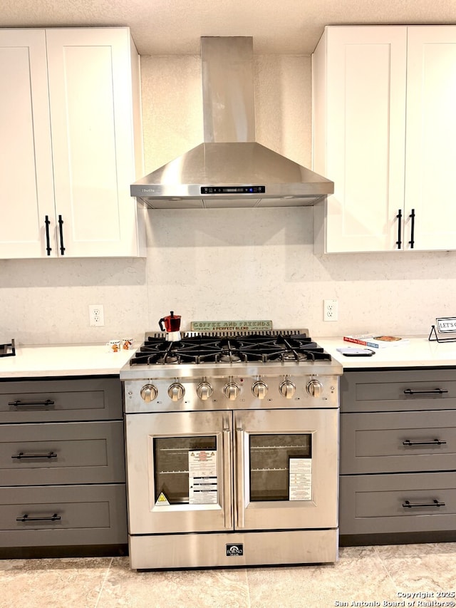 kitchen featuring backsplash, gray cabinetry, stainless steel range, wall chimney range hood, and white cabinets