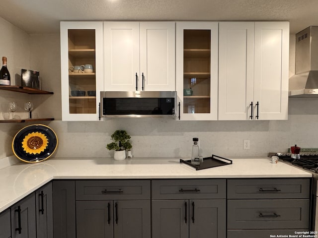 kitchen featuring wall chimney exhaust hood, gray cabinets, a textured ceiling, gas stove, and white cabinetry