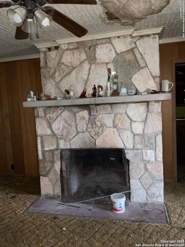 details featuring a stone fireplace, wood walls, crown molding, and ceiling fan